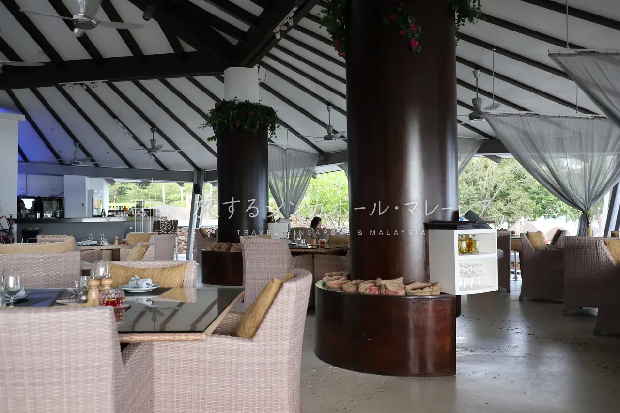 店内は高い寄棟天井とむき出しの太い柱、ラタンのソファ席。シーリングファンが回り、海風が抜ける開放的な空間です。