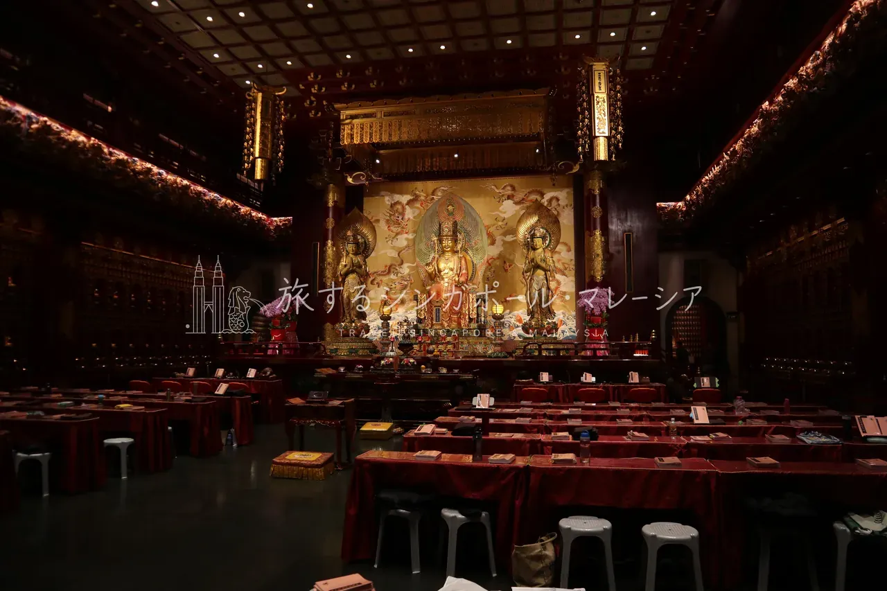 仏牙寺の本堂内部。金色に輝く三尊像を正面に、朱色の卓と座が整然と並び、外観に劣らず内部も荘厳。靴を脱いで静かに見学できます。