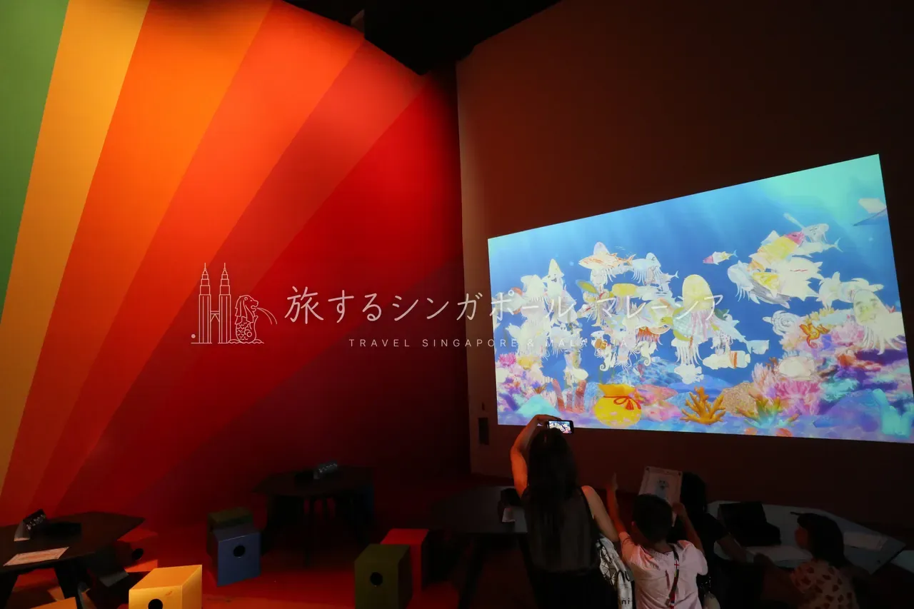左:ネオン色の街並みを描いた映像の暗室。右:虹色の光に満ちた水族館映像の空間で、来場者も思わずカメラを向けます。