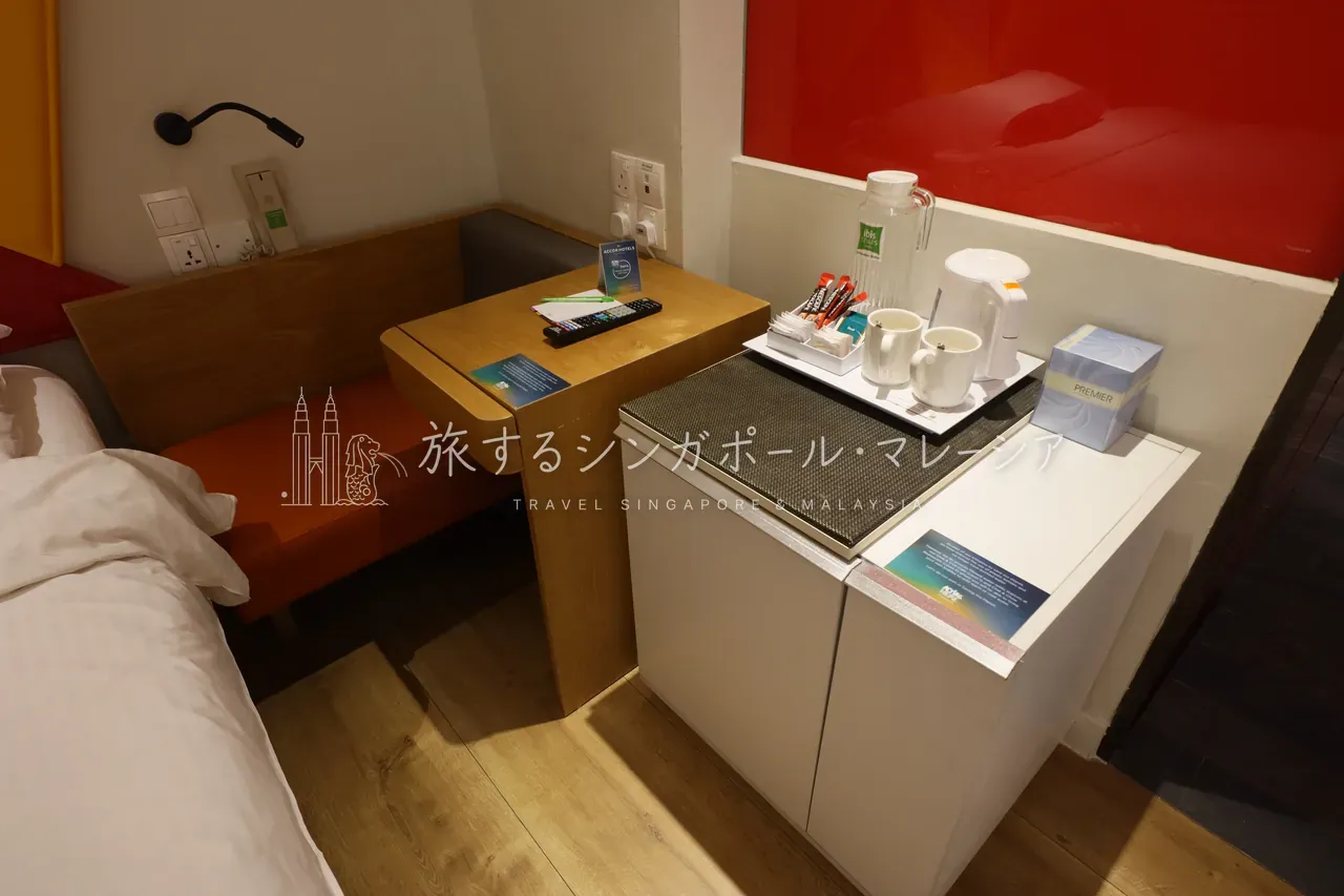 左：赤い光沢のアクセント壁とコンパクトにまとまった全景。右：オレンジの可動式サイドテーブルなど、差し色づかいが楽しい客室。