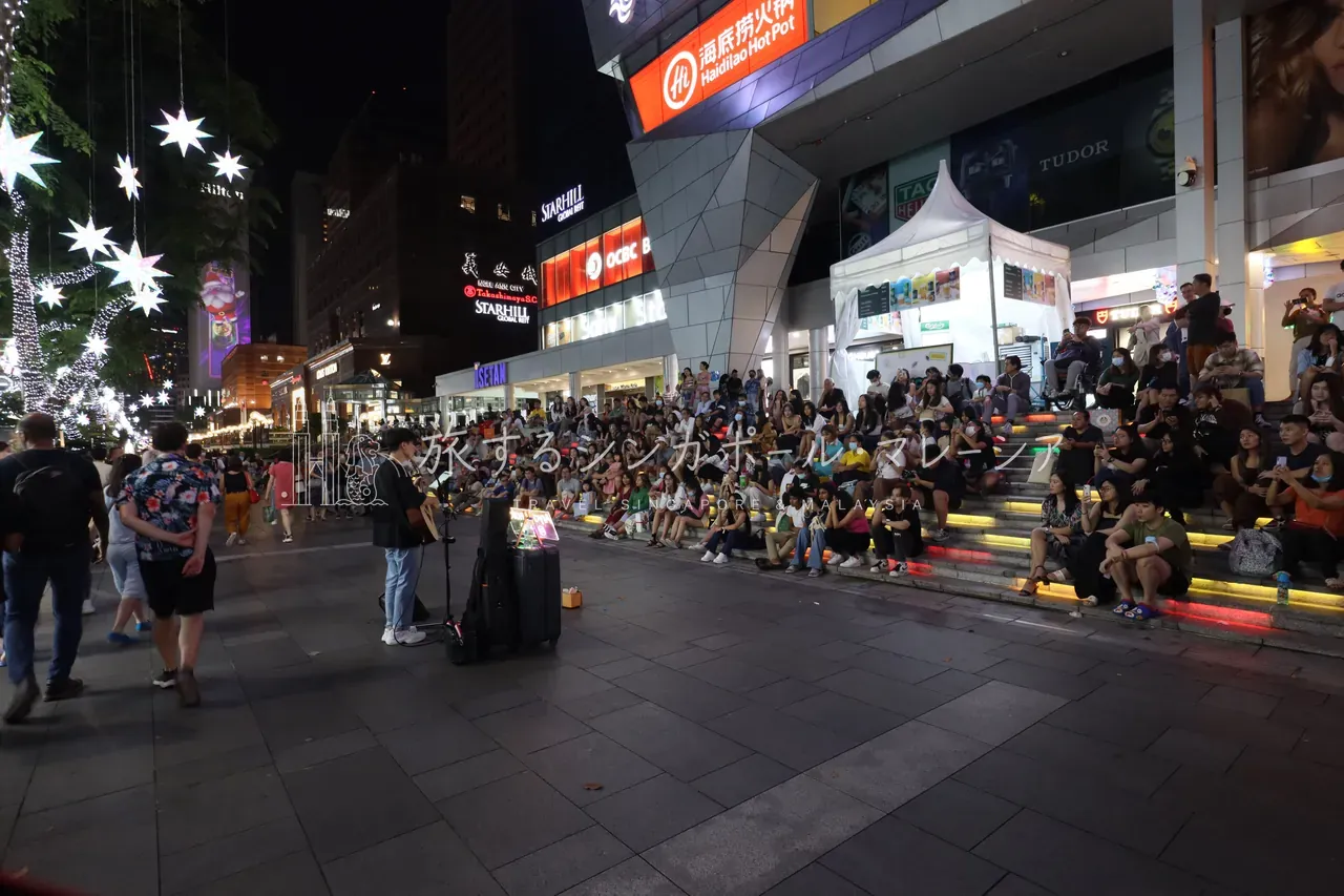 左：高島屋前の広場では、星形イルミネーションの下、階段に座った大勢の観客がストリートミュージシャンの演奏に聞き入っていました。右：パラゴン正面は青く輝くイルミネーションの壁と大きなクリスマスツリーで彩られ、入口にはGUCCIの大型広告。夜のオーチャードは華やかさが一段増します。