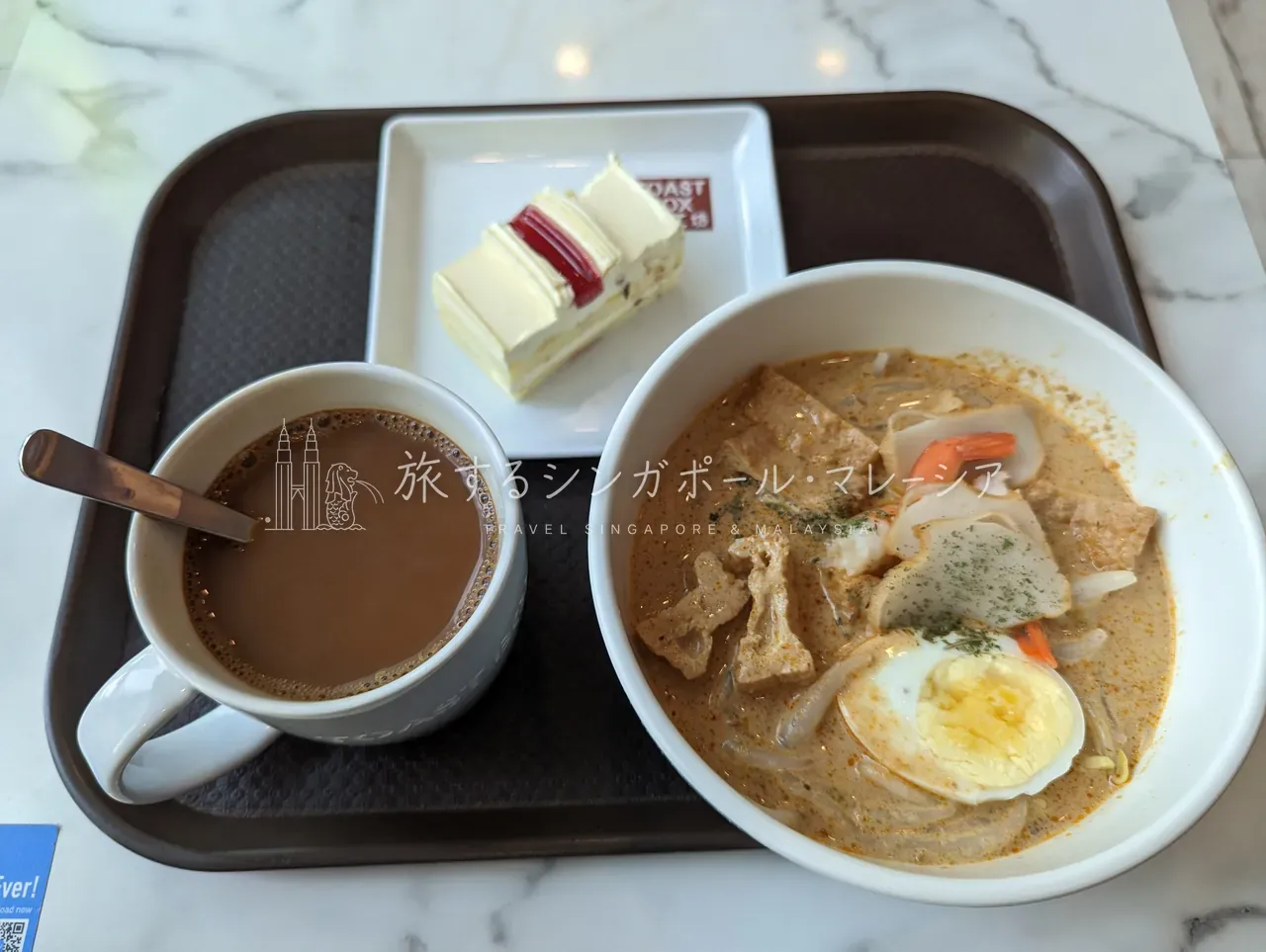 ラクサに、泡立つコピ（南洋コーヒー）とケーキを添えたセット。甘いも辛いもカフェ一軒で完結する手軽さ。